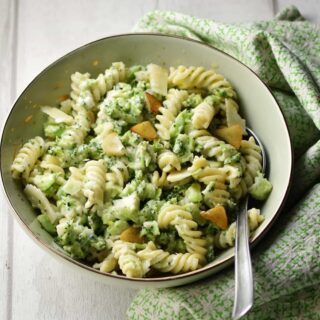 Broccoli pasta with spoon in light green coloured bowl wrapped in green cloth.