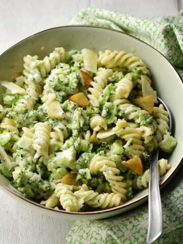 Broccoli pasta with spoon in light green coloured bowl wrapped in green cloth.