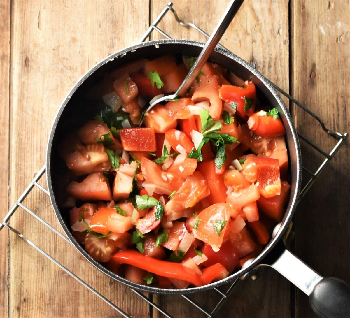 Chopped tomatoes, peppers and herbs in pot with spoon.