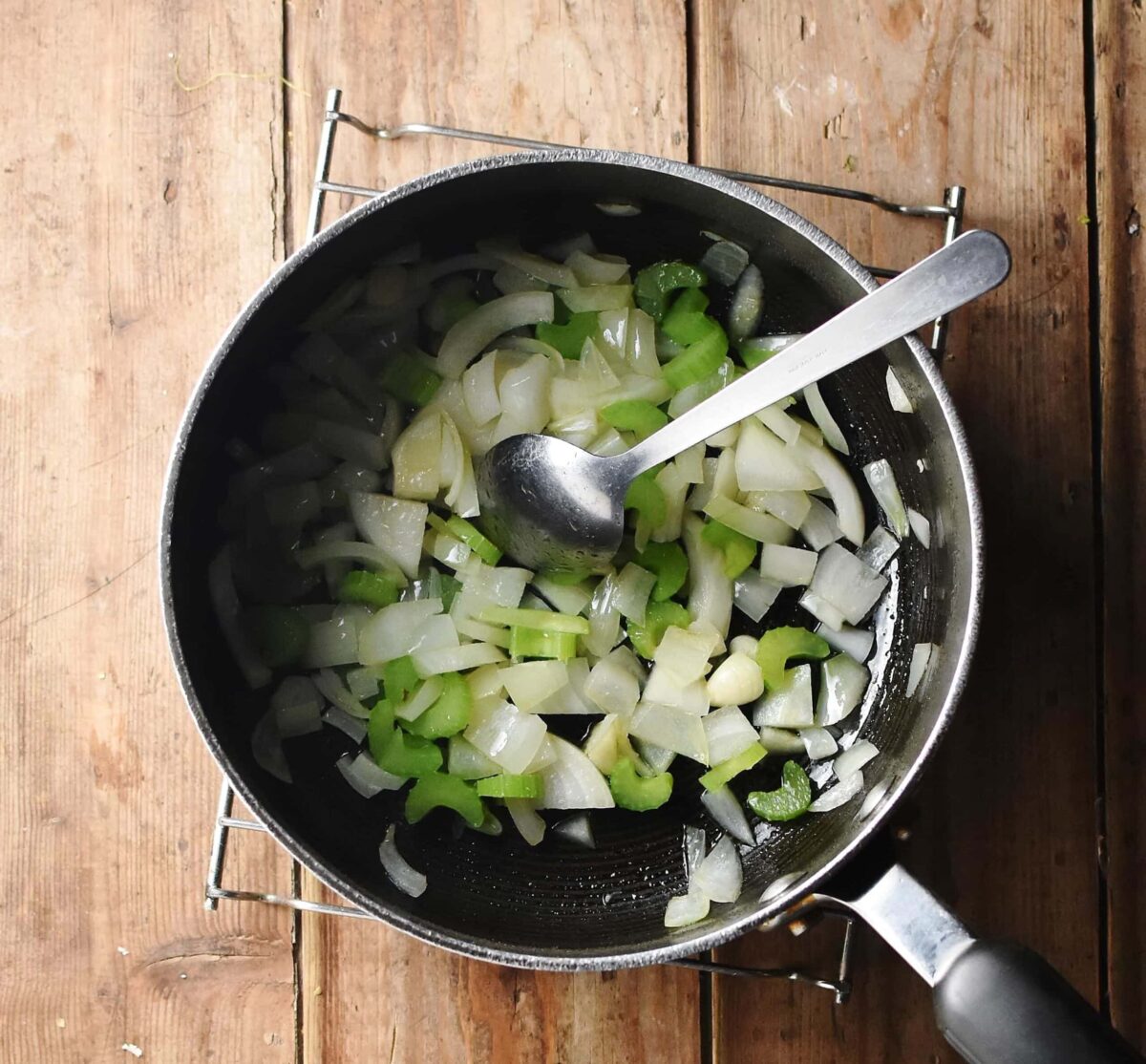 Chopped onions and celery in large pot with spoon.