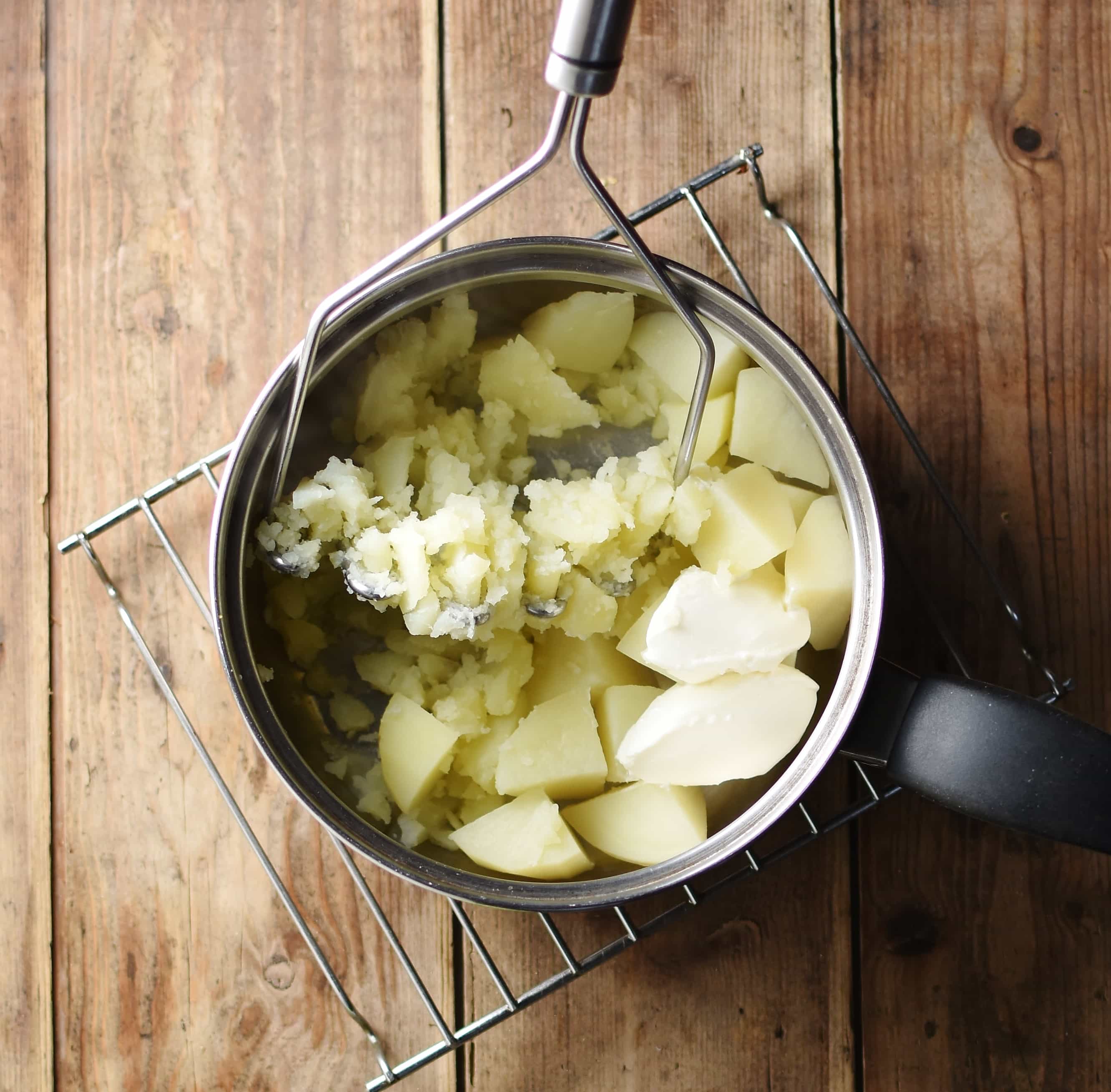 Potatoes in pot with potato masher.