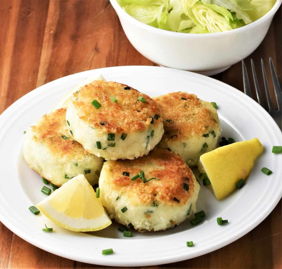 Side view of fried fish cakes with lemon wedges on plate.