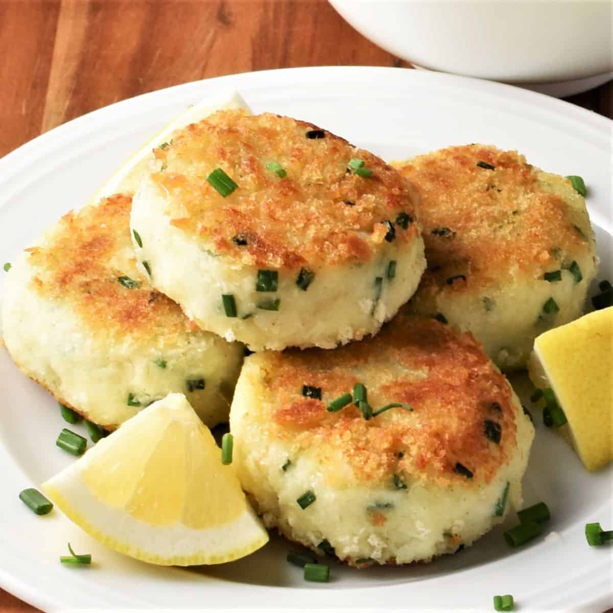 Close-up view of potato fish cakes with lemon wedges on white plate.