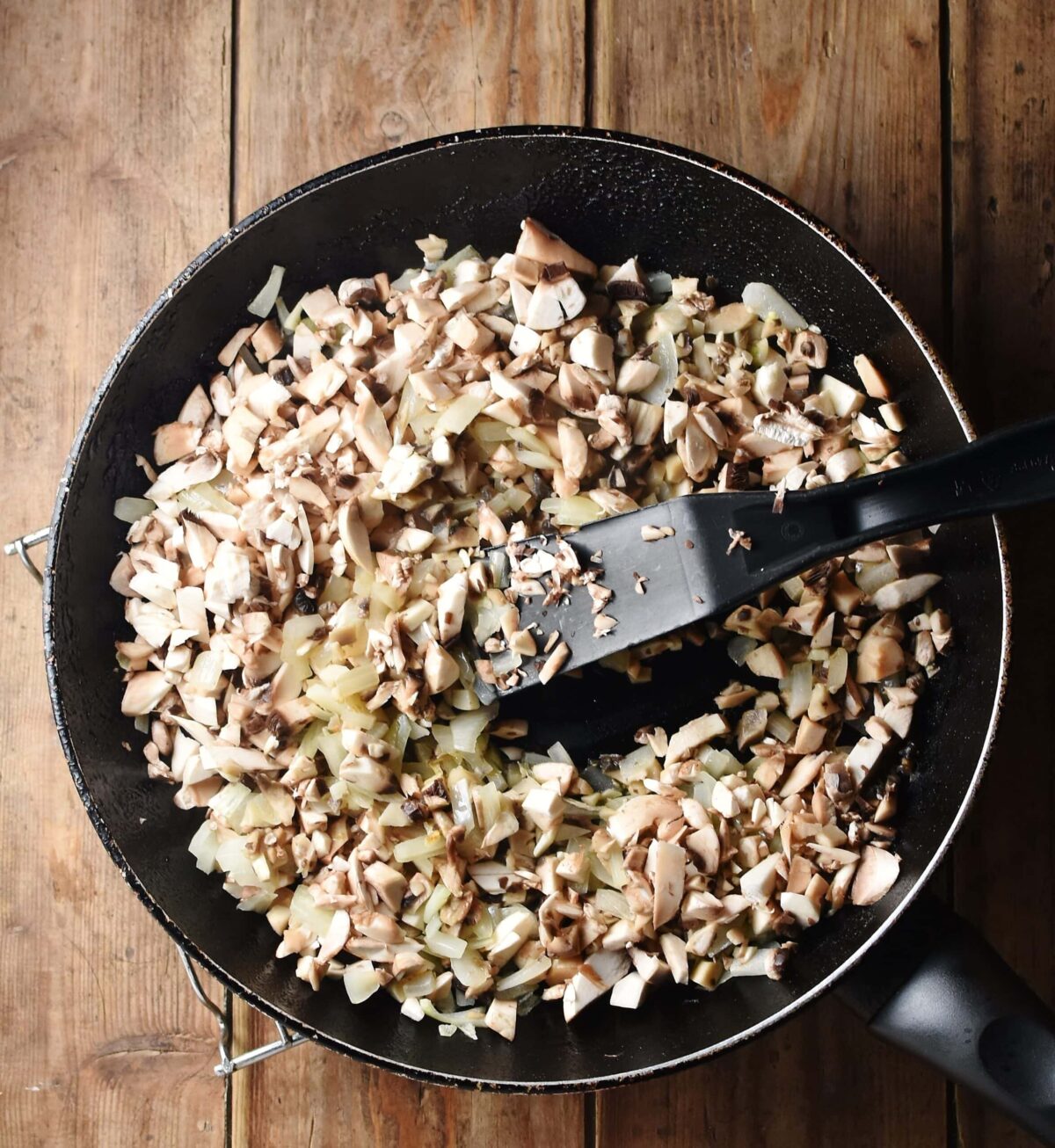 Chopped mushrooms and onion in skillet with black spatula.