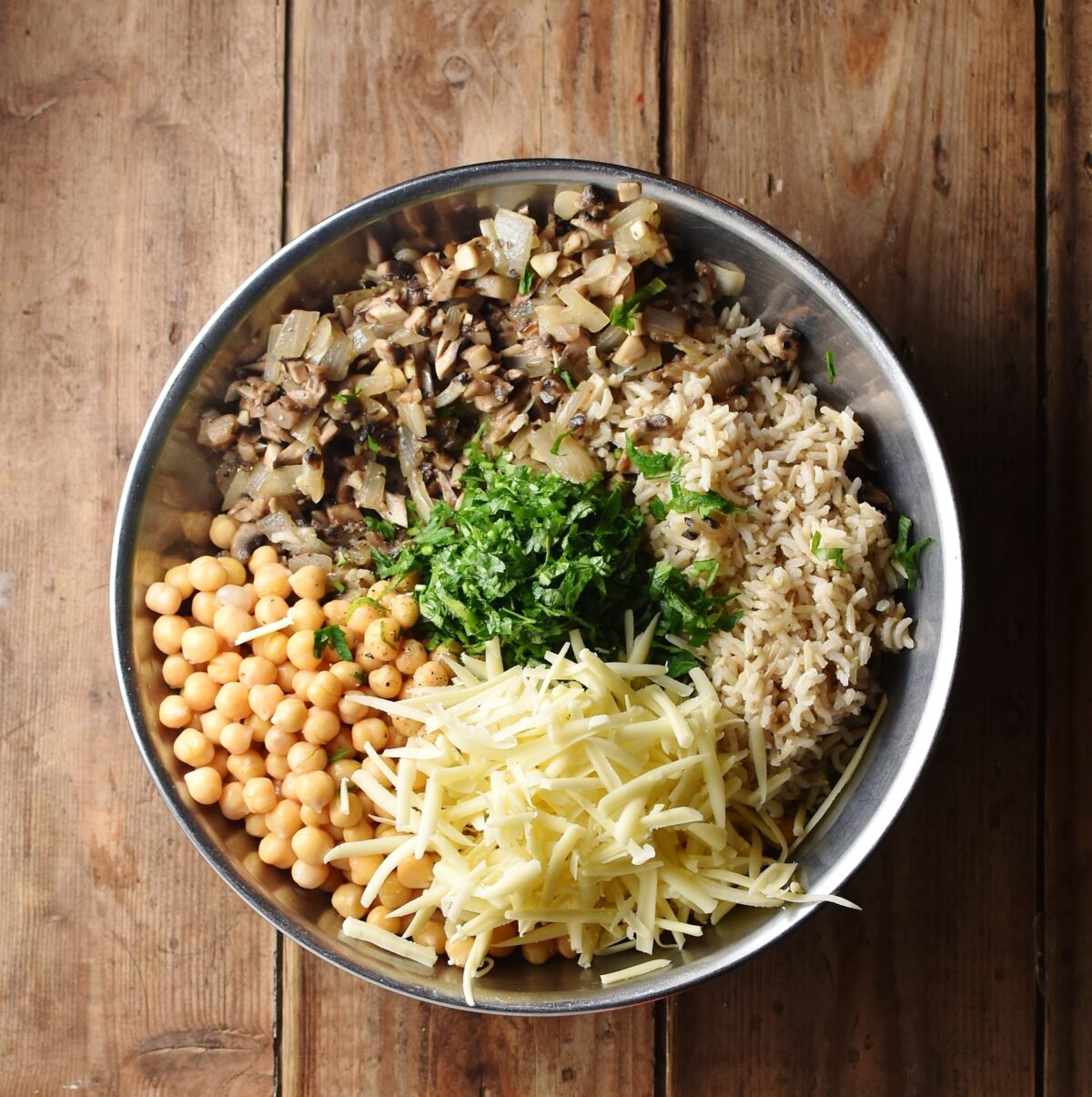 Chickpeas, mushrooms, brown rice, grated cheese and chopped herbs in large metal bowl.