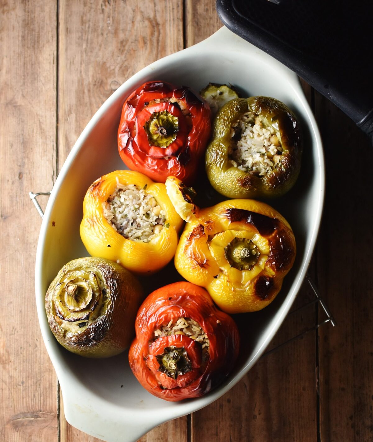 Top down view of baked tri-coloured stuffed peppers in oval dish. 
