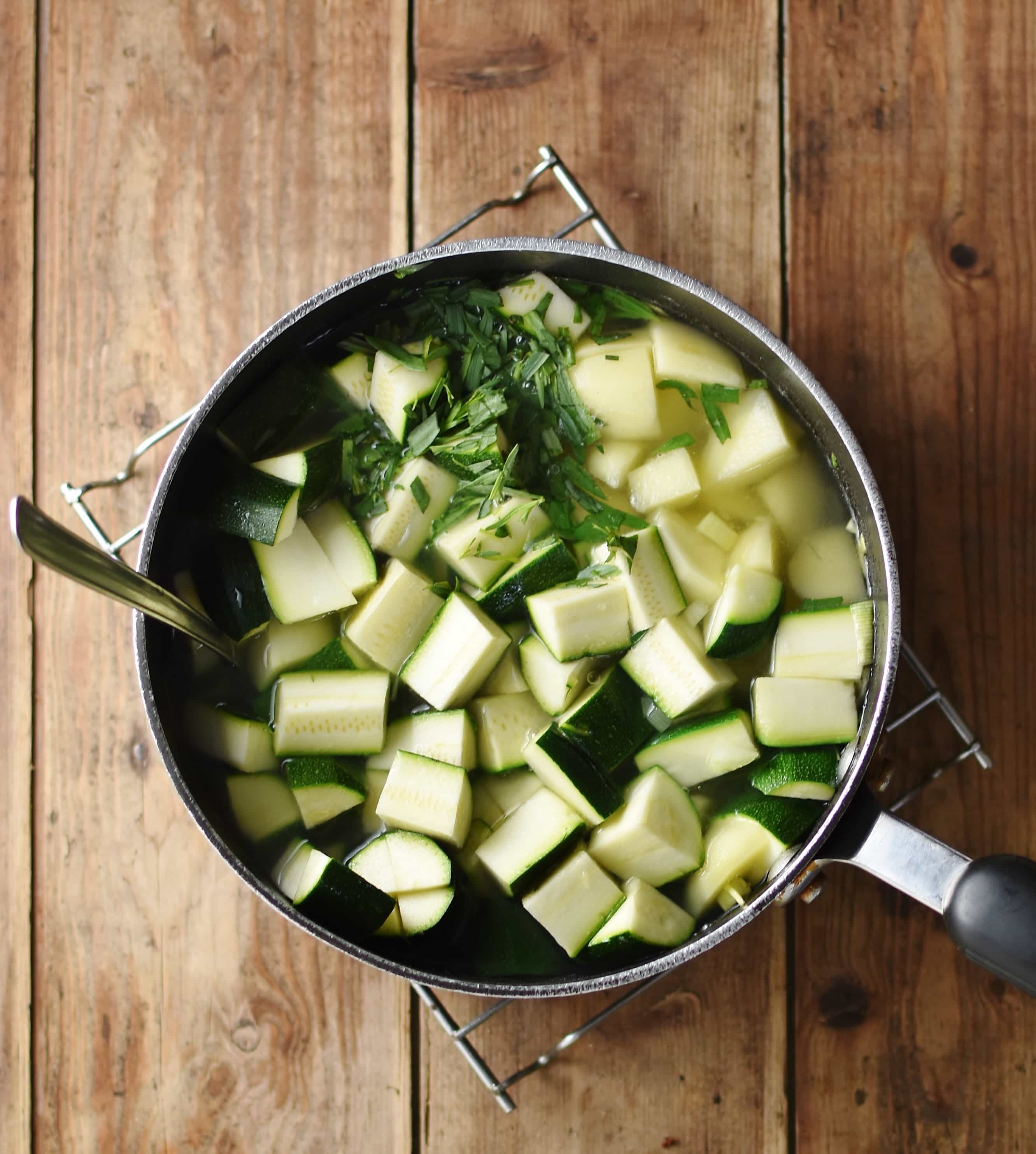 Cubed zucchini, potatoes and herbs in large pot filled with water.