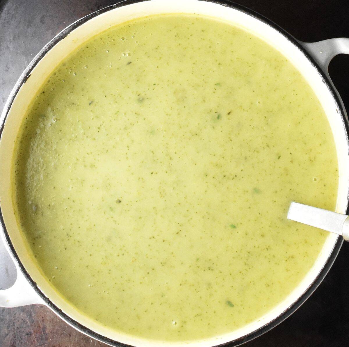 Top down view of creamy zucchini and potato soup in white pot with ladle.