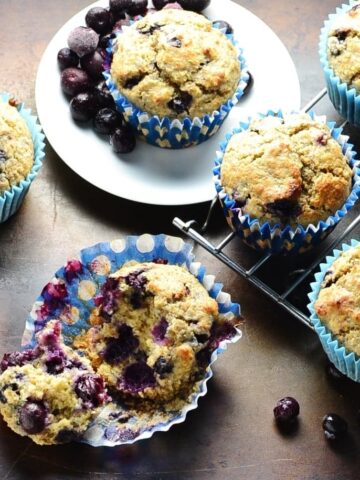 Top down view of blueberry muffins on oven tray with small white plate and cooling rack.