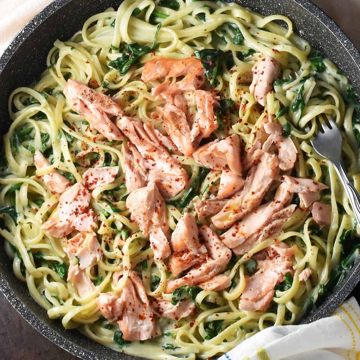Top down close-up view of creamy salmon pasta with spinach in large, shallow pan.