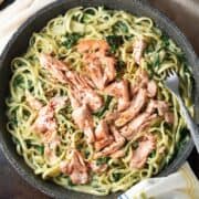 Top down view of salmon spinach pasta in large shallow pan with fork.