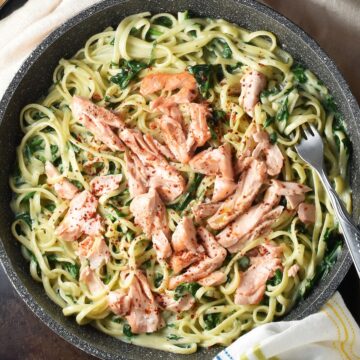 Top down view of salmon spinach pasta in large shallow pan with fork.