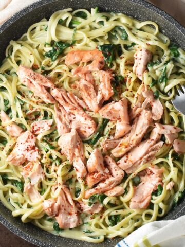 Top down view of salmon spinach pasta in large shallow pan with fork.