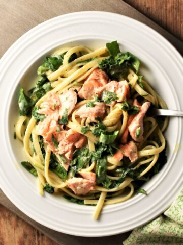 Salmon and spinach with pasta and creamy sauce in white bowl with fork.