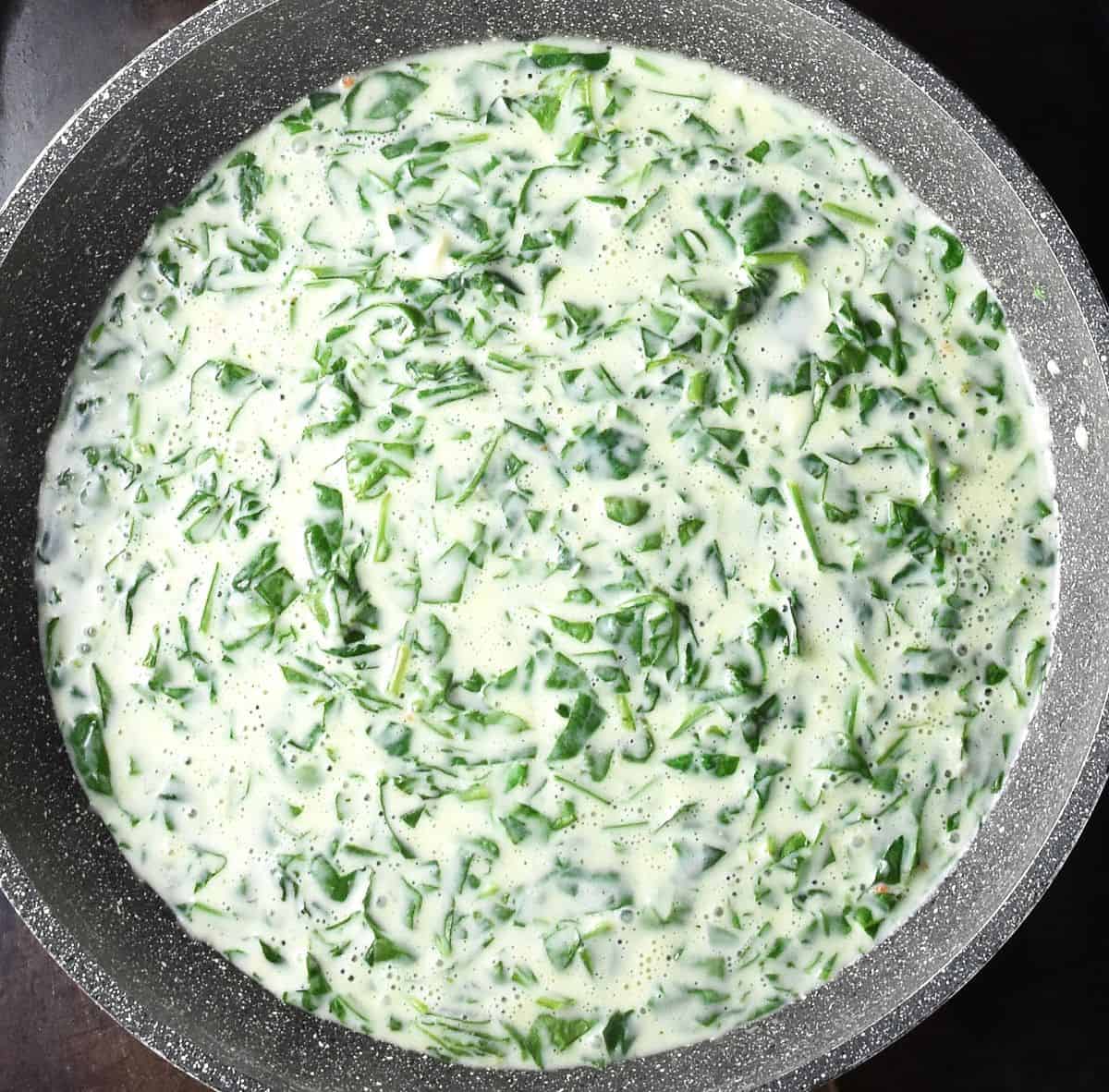 Creamy sauce with spinach in large, shallow pan.