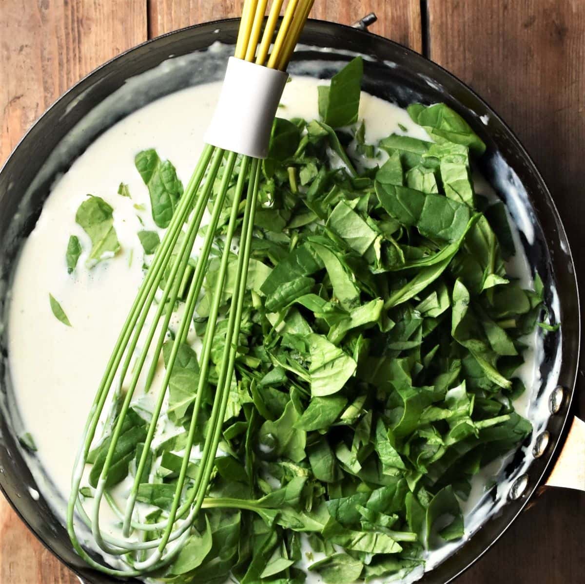 Whisking fresh, chopped spinach into creamy sauce in large pan.