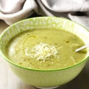 Side view of creamy zucchini potato soup in green bowl with spoon.