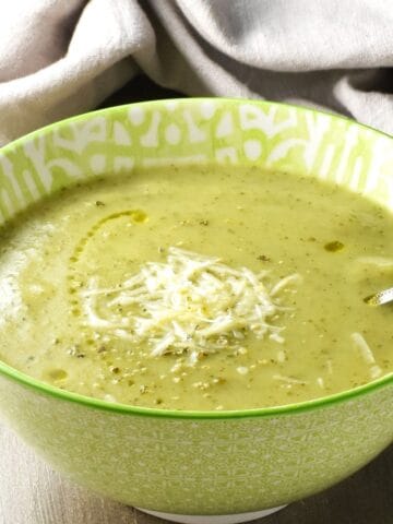 Side view of creamy zucchini potato soup in green bowl with spoon.