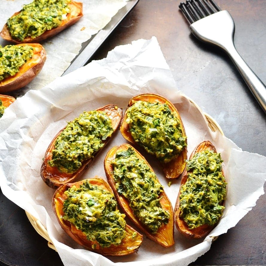 Top down view of stuffed sweet potatoes with spinach in basket lined with white paper and cooking brush next to it.