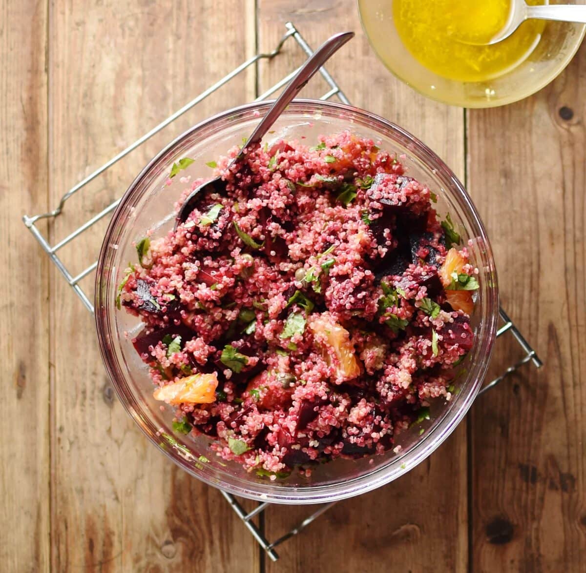 Top down view of quinoa beetroot salad with spoon inside large bowl, with dressing in small dish in top left corner.