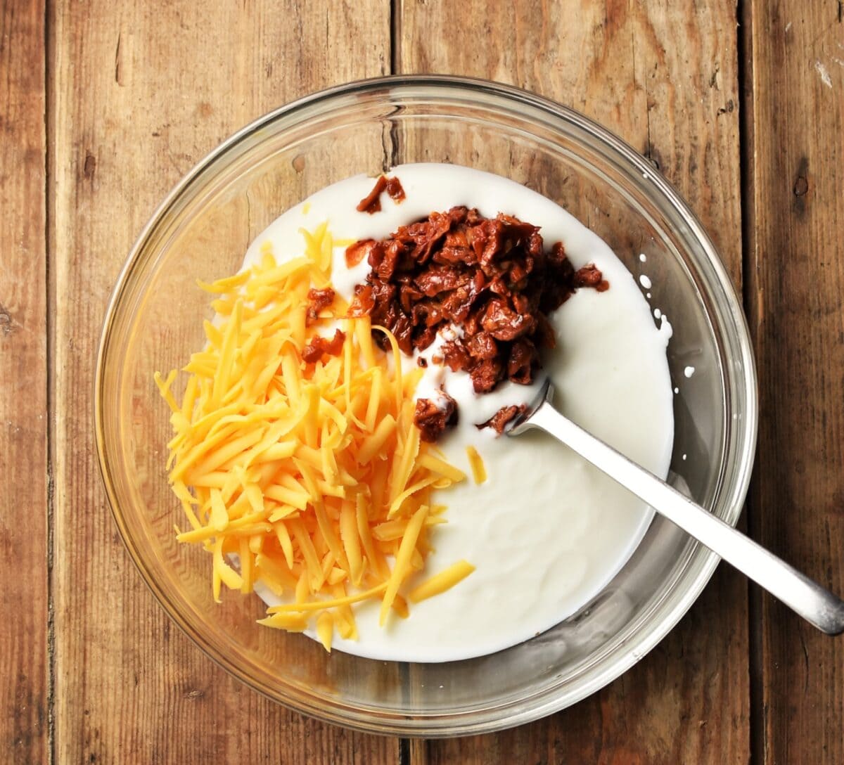 Grated cheese, buttermilk and chopped sun dried tomatoes in mixing bowl with fork.