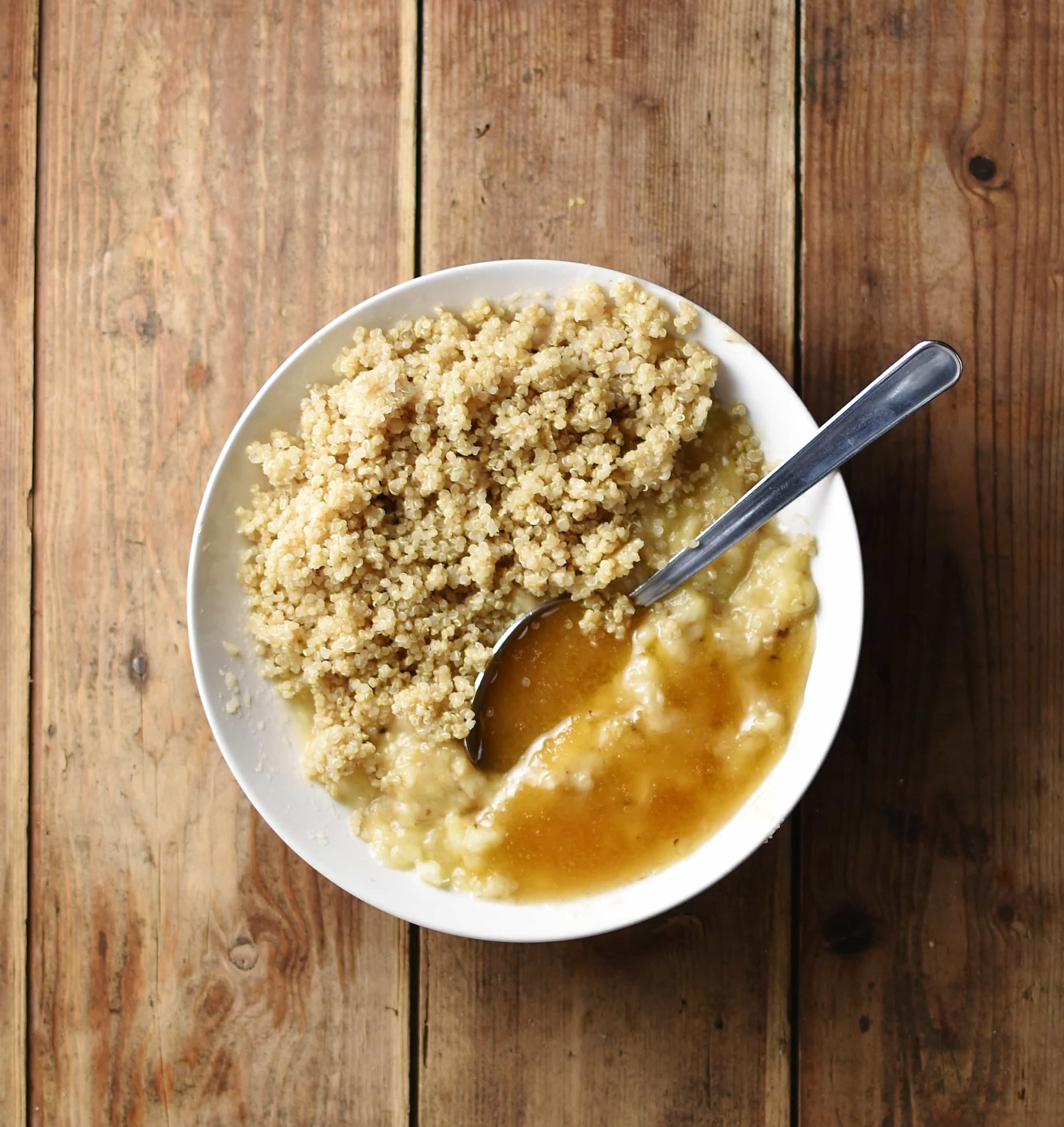 Cooked quinoa with mashed banana and honey in white bowl with spoon.