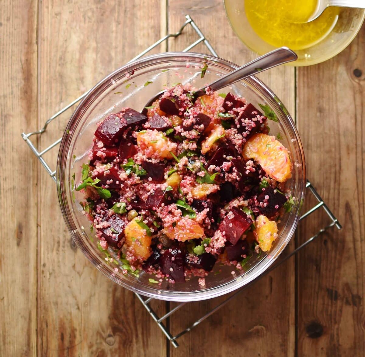 Beets, quinoa and orange salad with spoon inside translucent bowl with salad dressing in small dish in top right corner.
