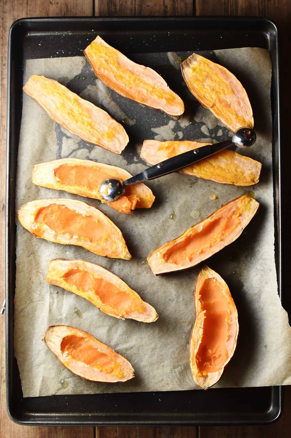 Sweet potato halves with melon baller on top of baking tray lined with paper.
