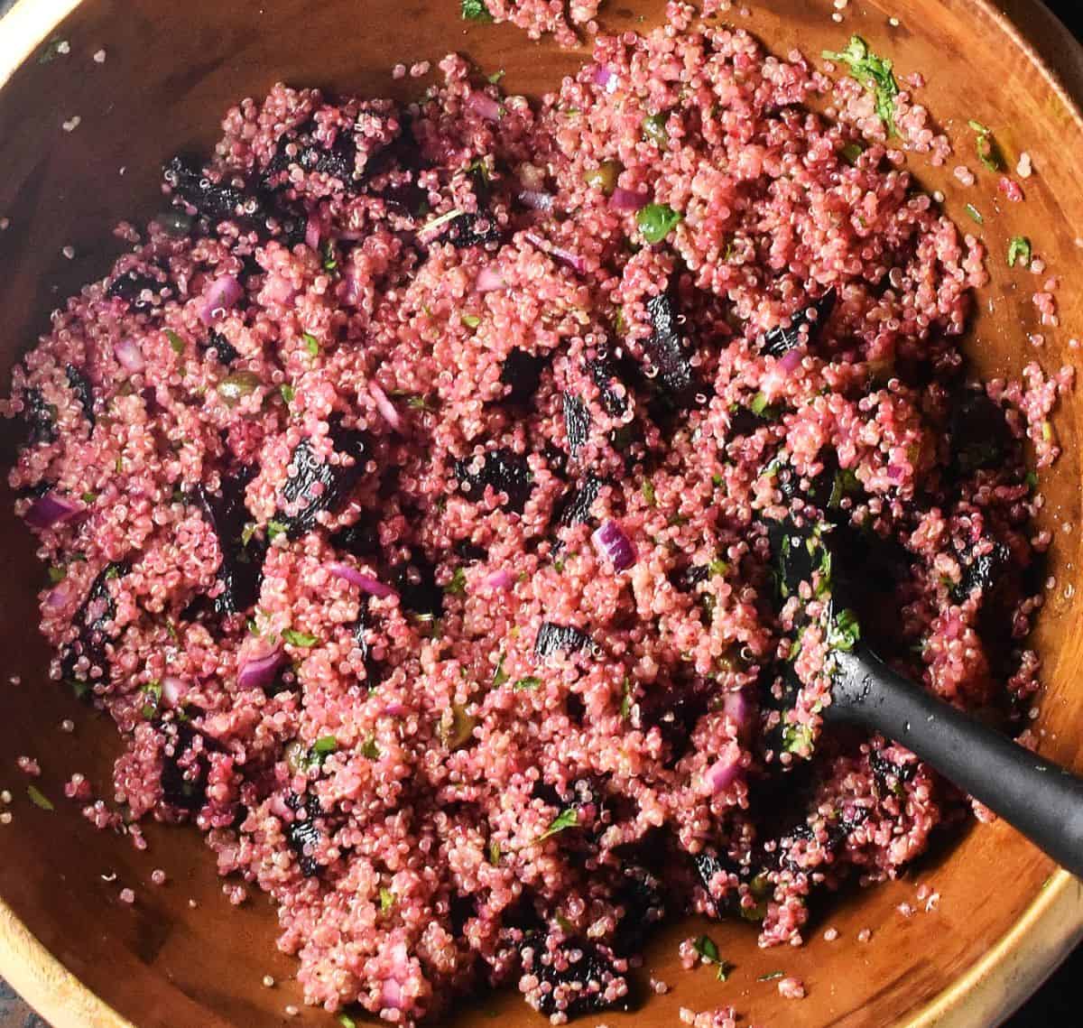 Top down view of beet and quinoa salad mixture in wooden bowl with black spatula.