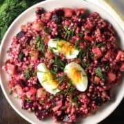 Top down view of pink coloured buckwheat salad on pink plate with dill in background.