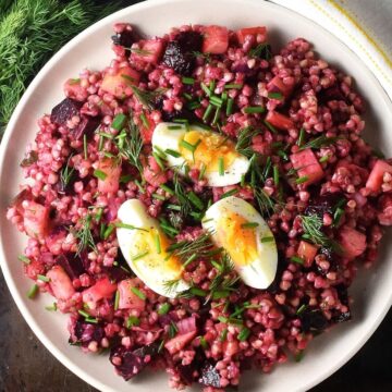 Top down view of pink coloured buckwheat salad on pink plate with dill in background.