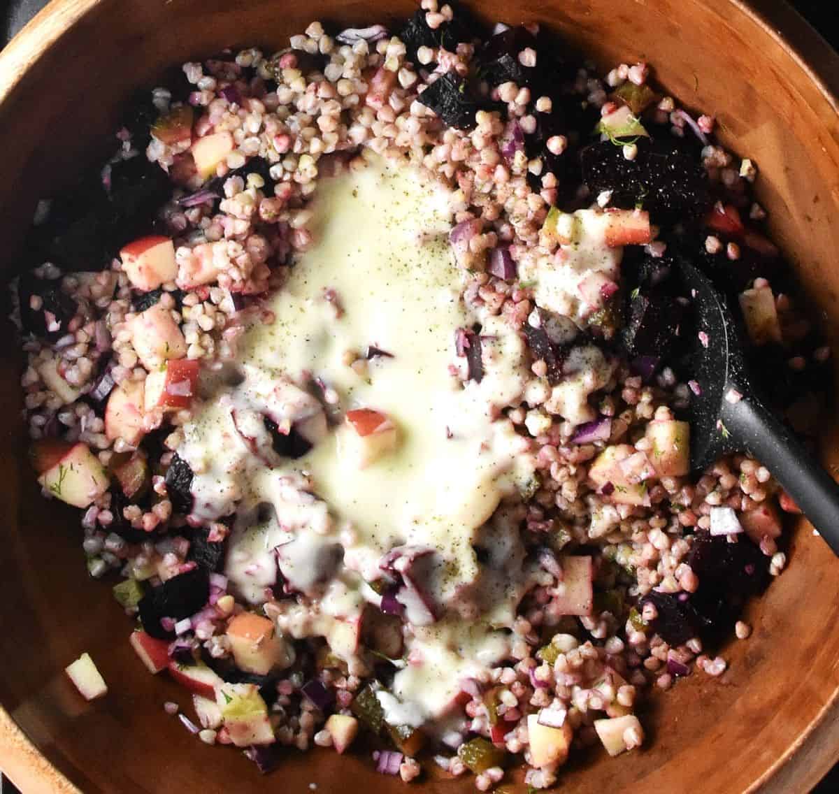 Top down view of buckwheat salad with creamy dressing in wooden bowl.