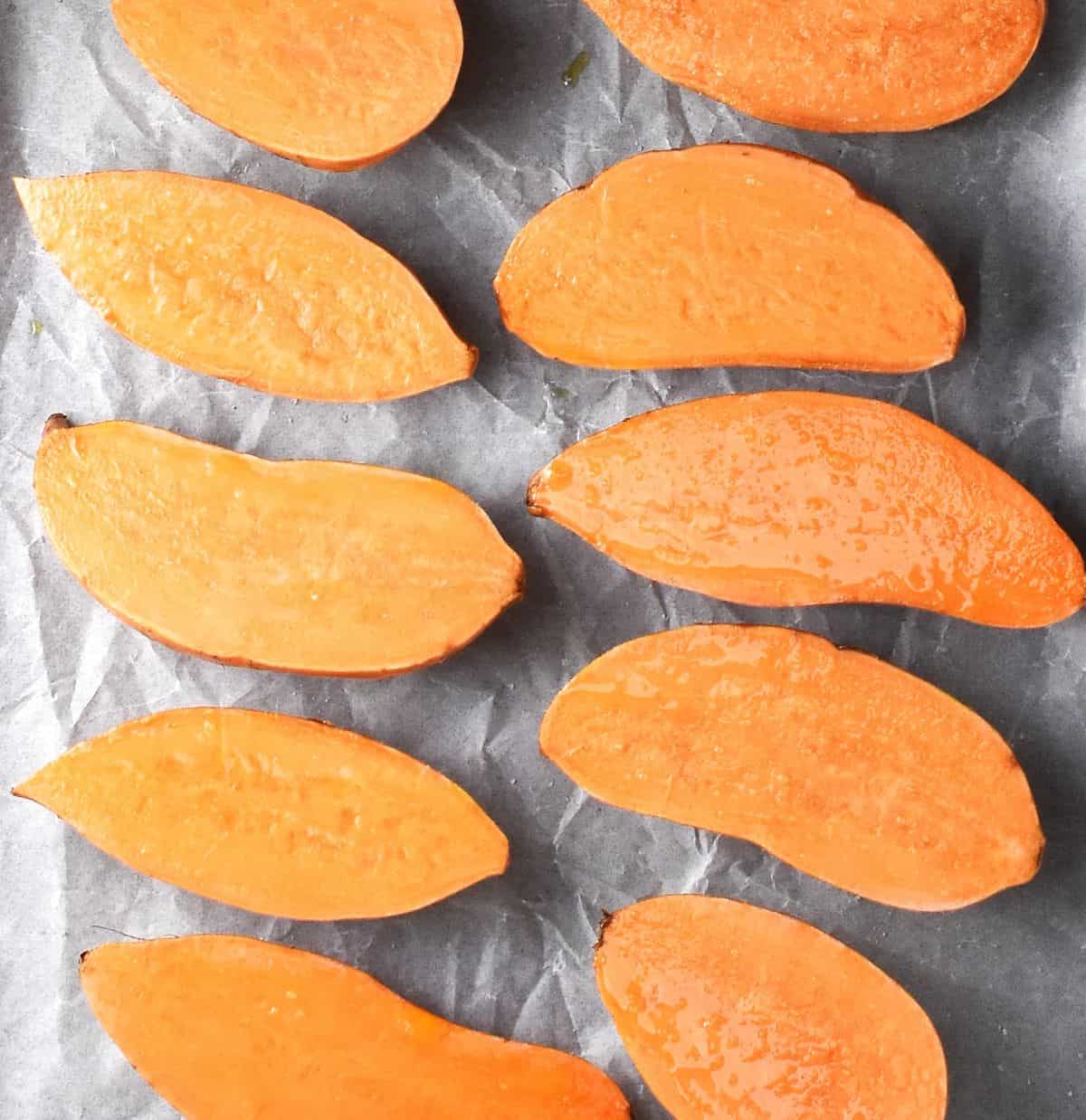 Top down view of uncooked sweet potato halves on parchment paper.