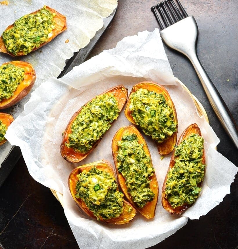 Top down view of stuffed sweet potatoes with spinach in basket lined with white paper and cooking brush next to it.