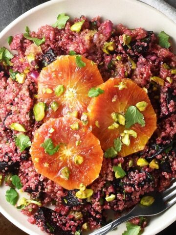Top down view of quinoa and beet salad with 3 orange slices on top on pink plate.