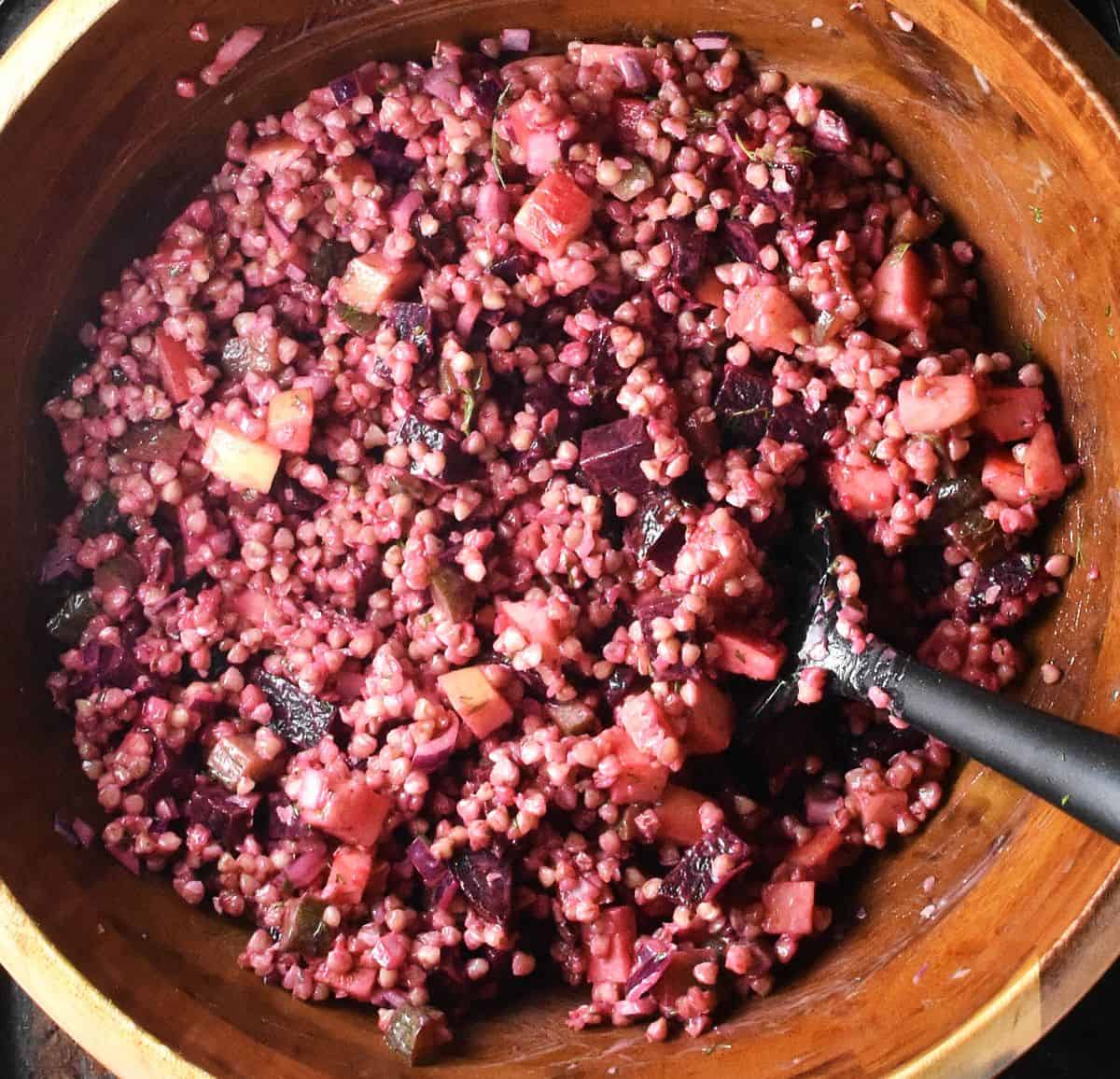 Pink coloured buckwheat salad in large wooden bowl with black spoon.