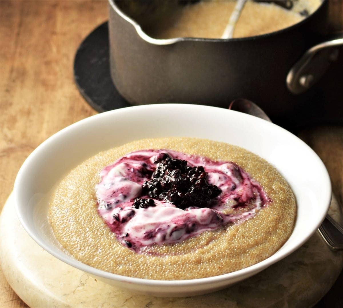 Side view of amaranth porridge with yogurt and fruit in white bowl.