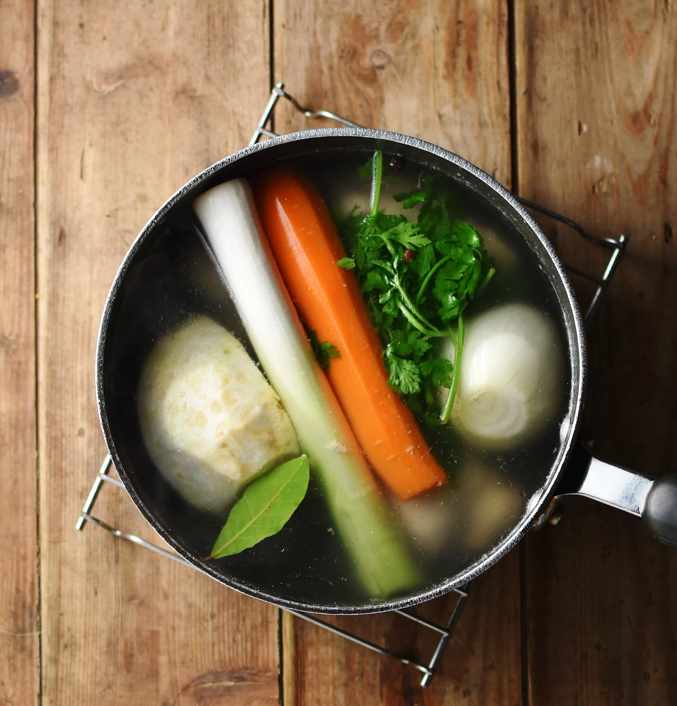 Whole, peeled carrot, onion, leek and celeriac with bay leaf and parsley in large pot with water.