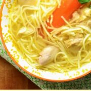 Chicken noodle soup with carrot in bowl with yellow pattern on top of green cloth.
