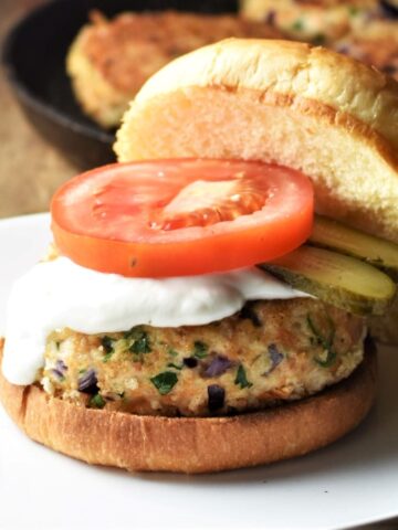 Chicken burger in open bun with sauce, slice of tomato and pickles.