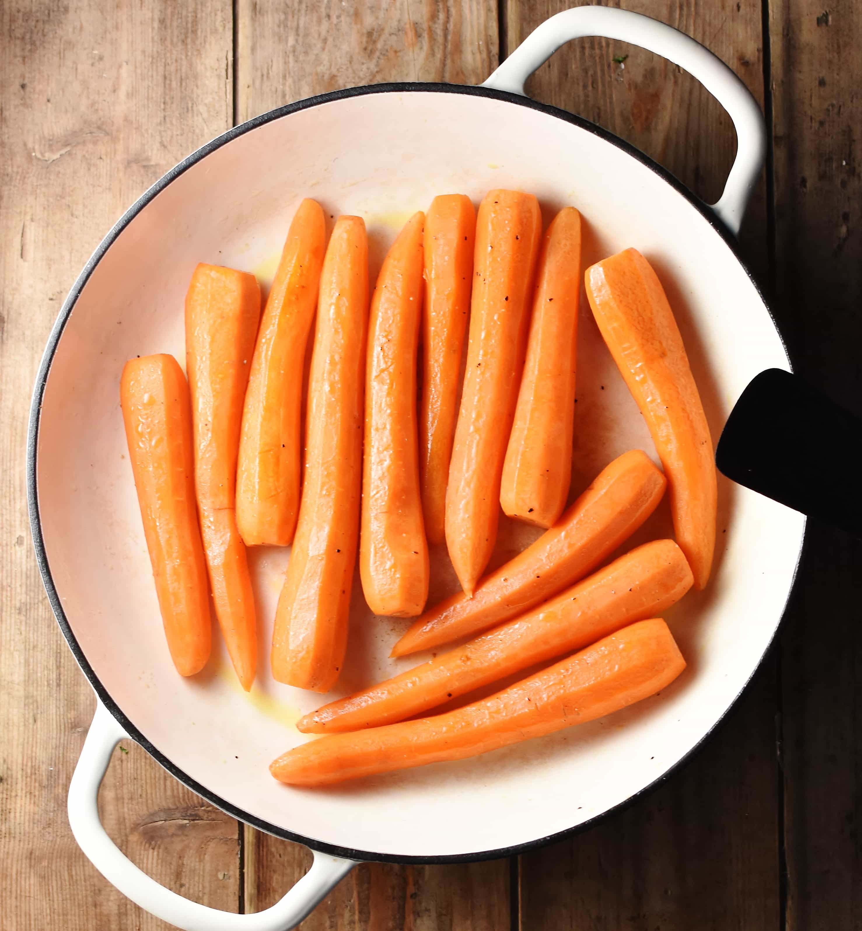 Peeled carrots in large shallow white pan with black spatula to the right.