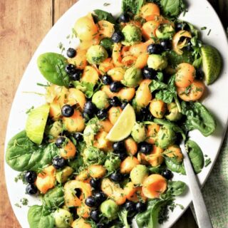 Top down view of cantaloupe salad with spinach and avocado on white oval plate with spoon.