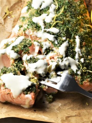 Close-up view of salmon with herbs and creamy sauce on top of parchment.