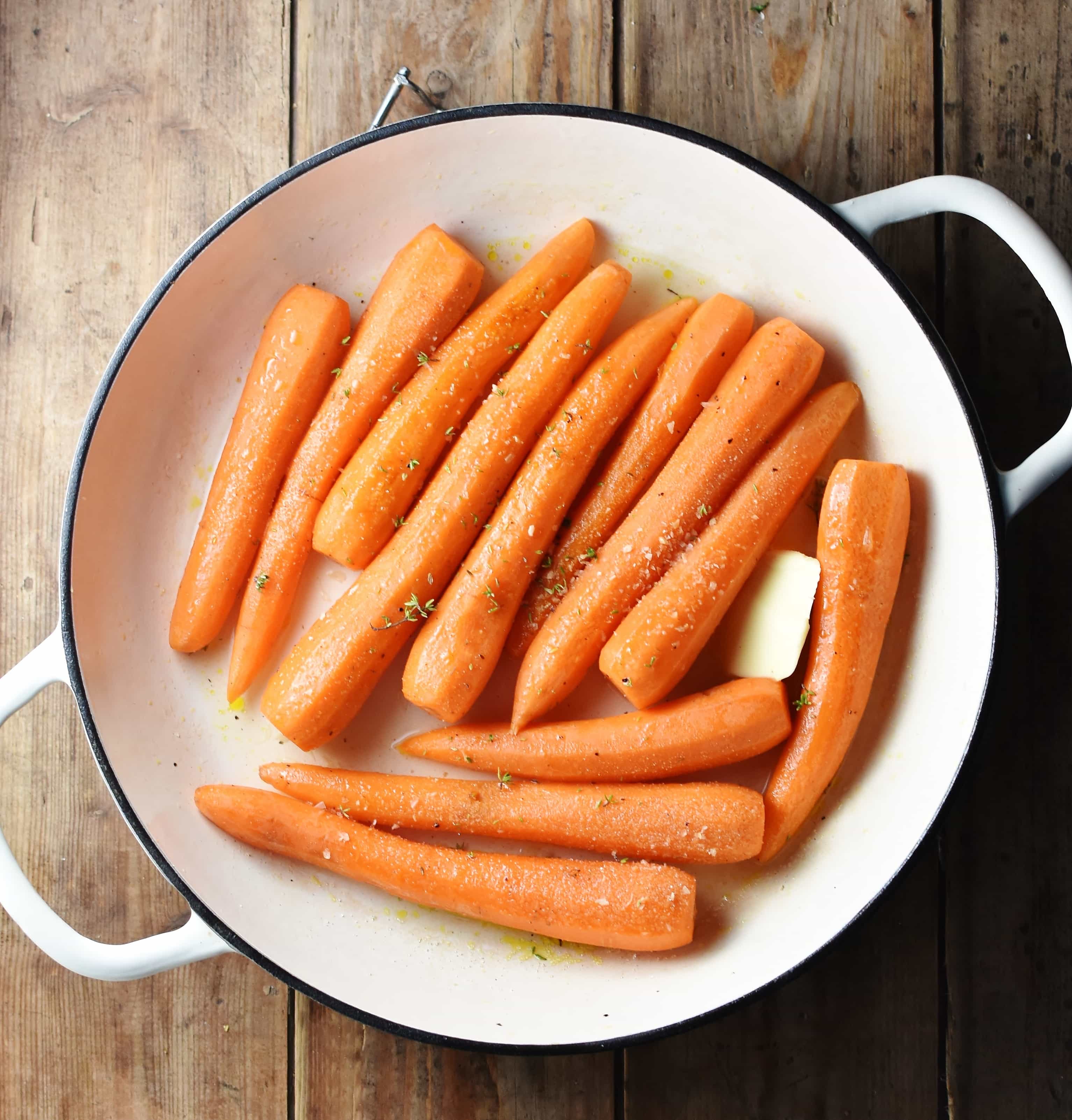 Braised carrots with knob of butter and seasoning in large white pan.