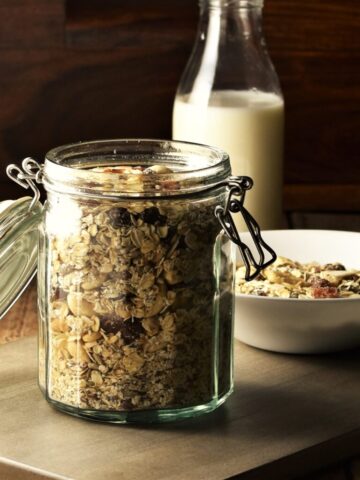 Homemade muesli in open jar, with bottle of milk and muesli in bowl in background.