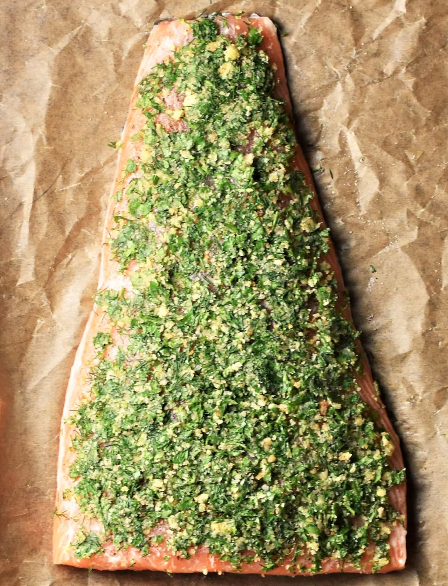 Salmon fillet topped with herb mixture on top of parchment.