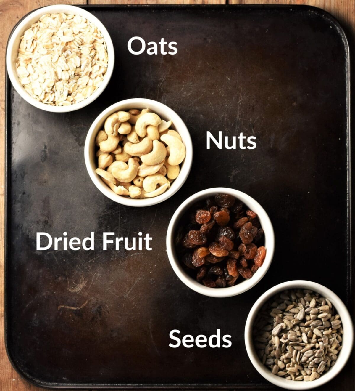 Top down view of oats, cashews, raisins and sunflower seeds in individual dishes.