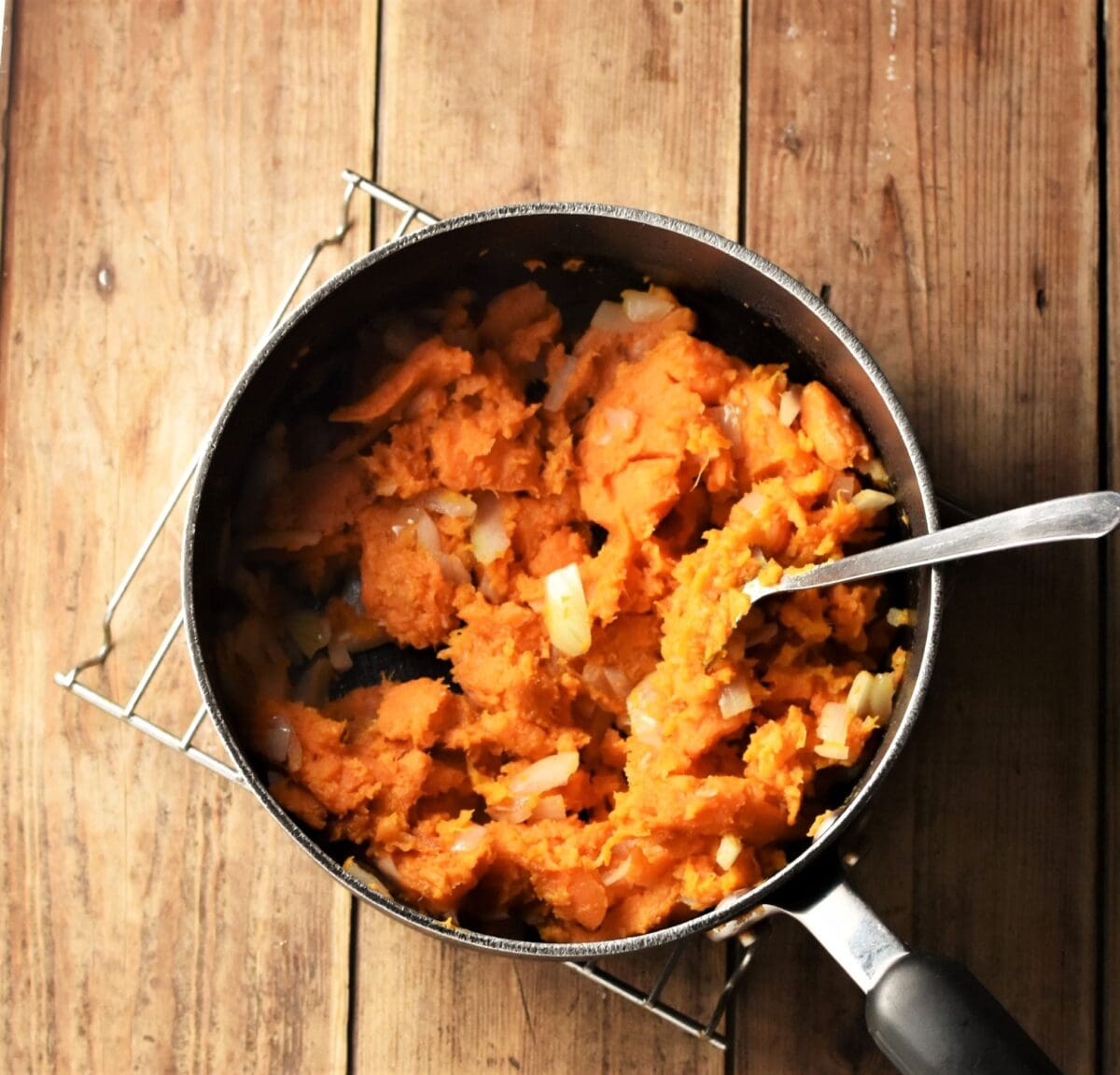 Sweet potato mash with chopped onions in large pot with spoon.