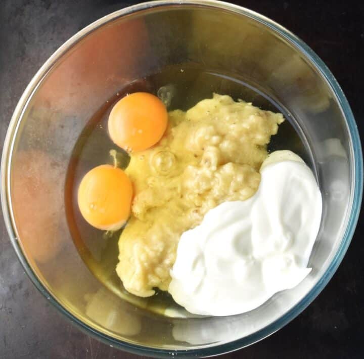 Eggs, mashed banana and yogurt in glass bowl.