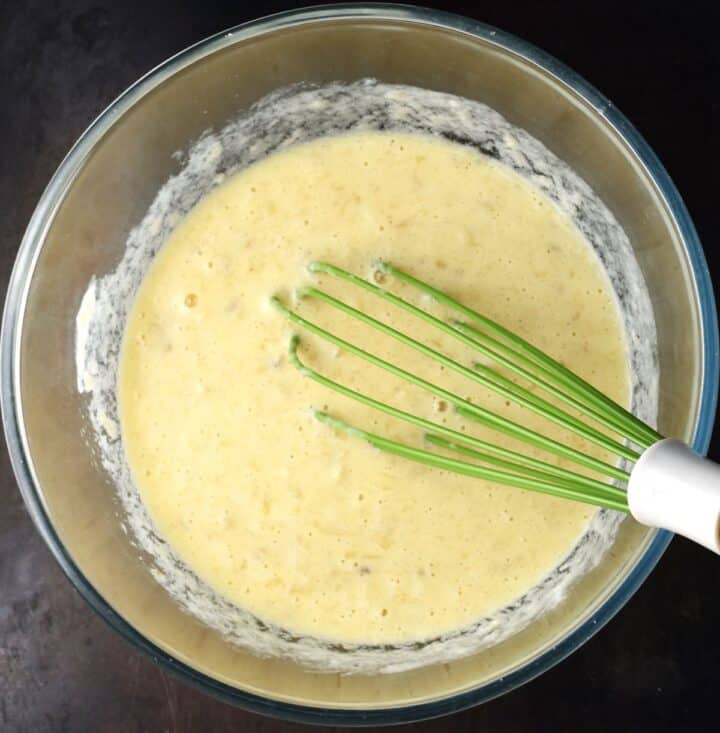 Wet mixture for banana and yogurt pancakes in glass bowl with whisk.